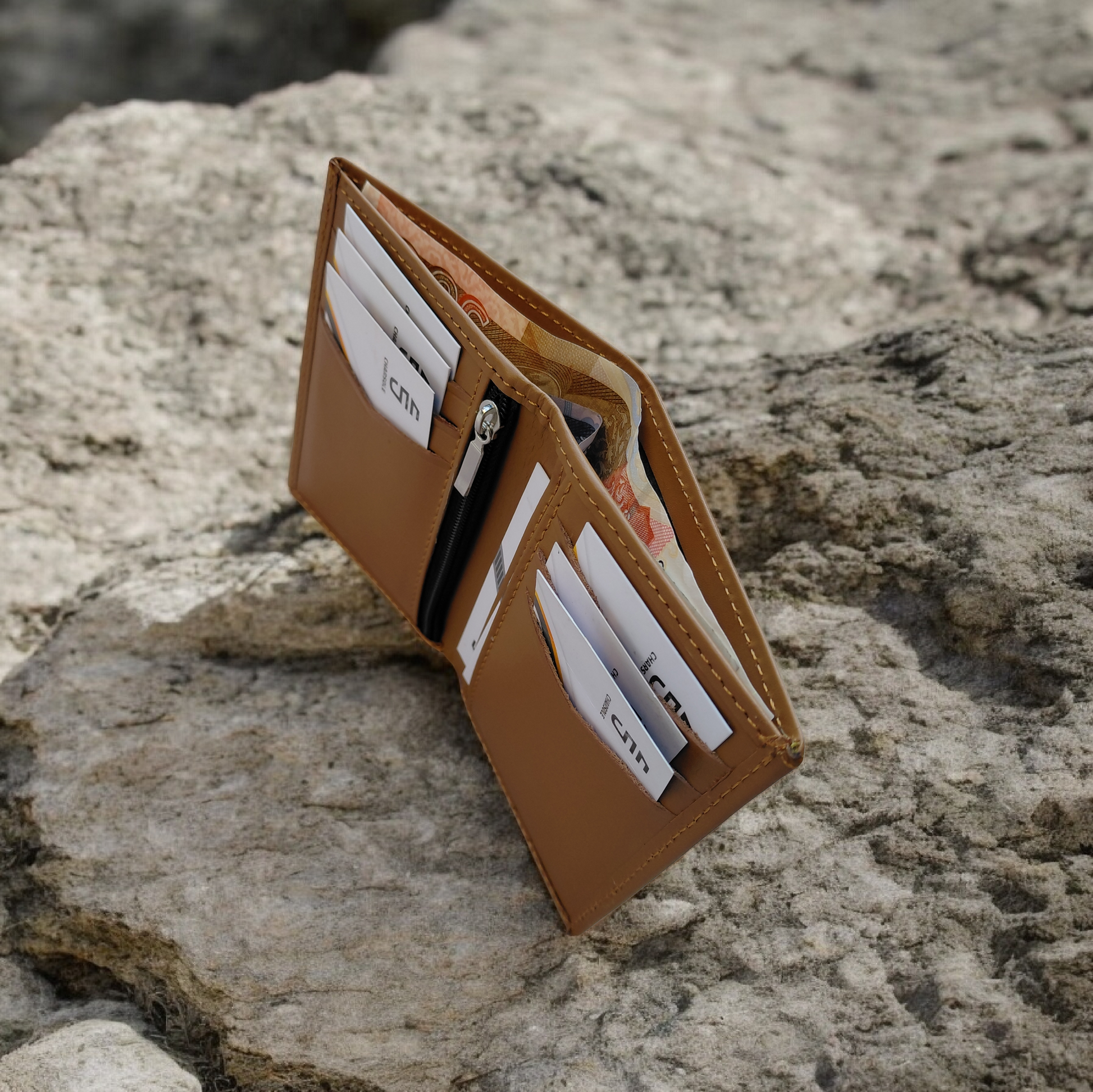 Brown leather wallet with card slots on a rocky surface